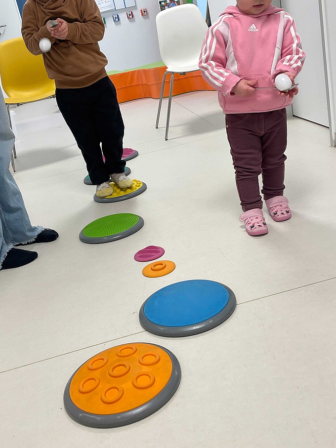 Eierlauf: Zwei Kinder balancieren Eier auf einem Löffel und gehen dabei einen Parcours aus Trittsteinen ab.