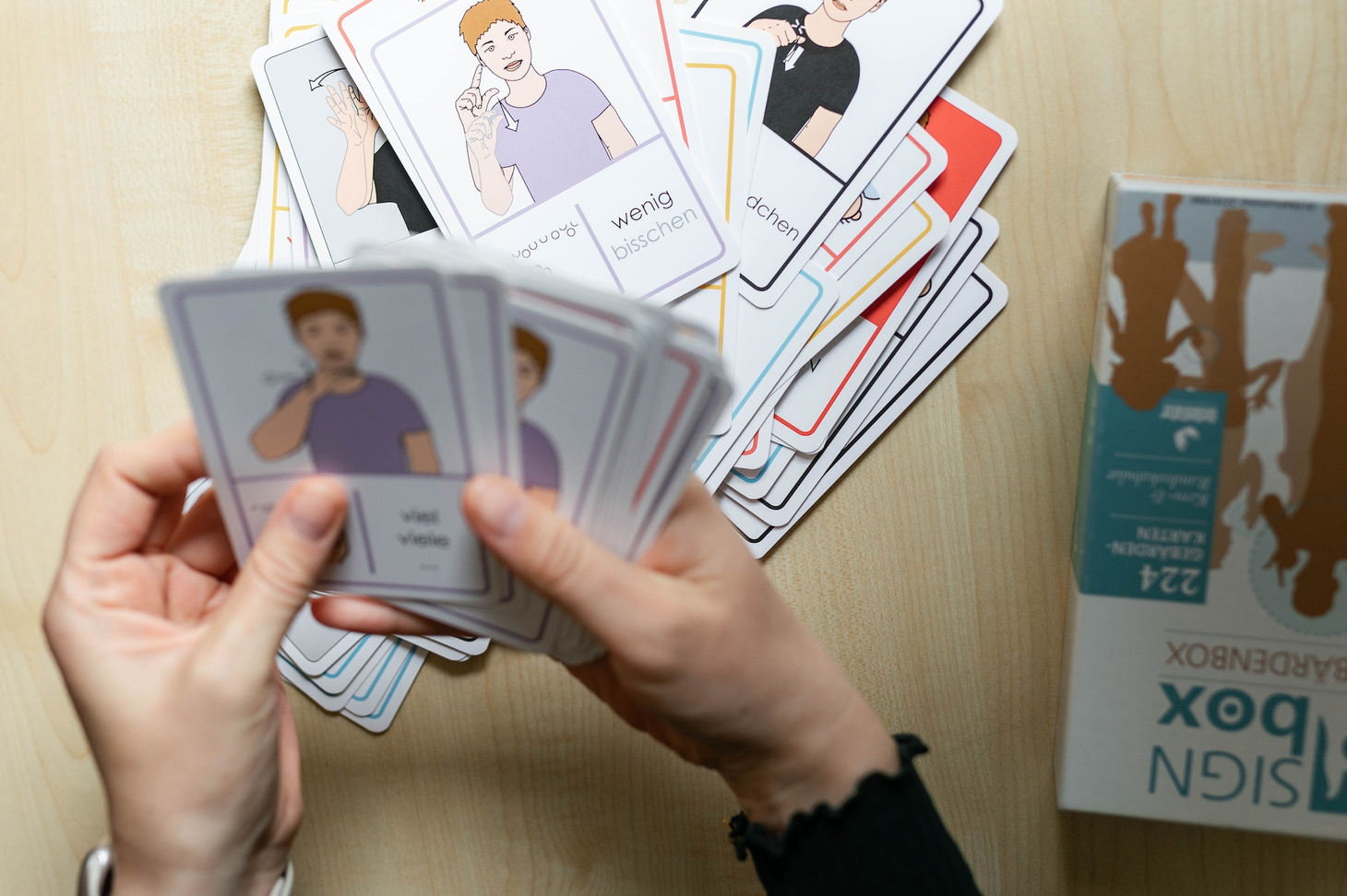 Gebärdenkarten liegen auf einem losen Haufen und werden in der Hand aufgefächert.