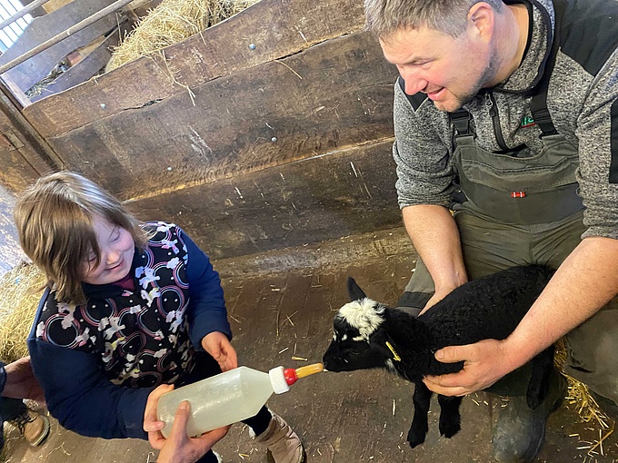 Eine Schülerin füttert ein Lämmchen mit einer Nuckelflasche.