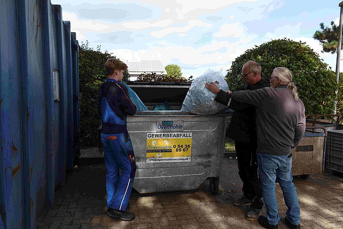 Timon Eichhorn und Thomas Hilgen schmeißen Müllsäcke in einen Müllcontainer.