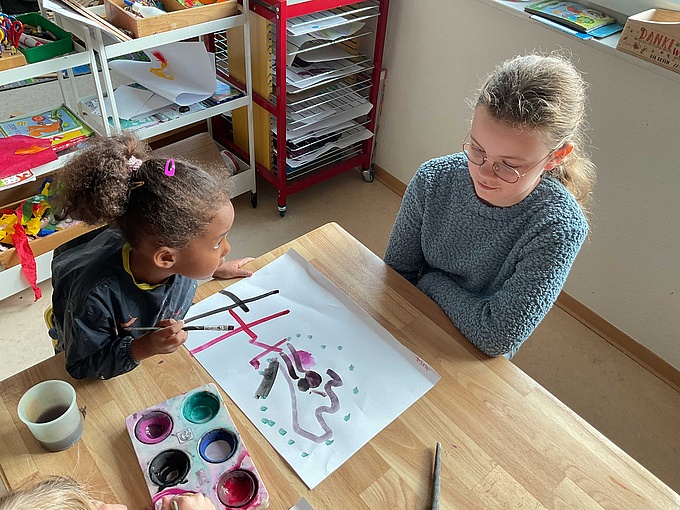 Eine Schülerin malt mit einem Kita-Kind.
