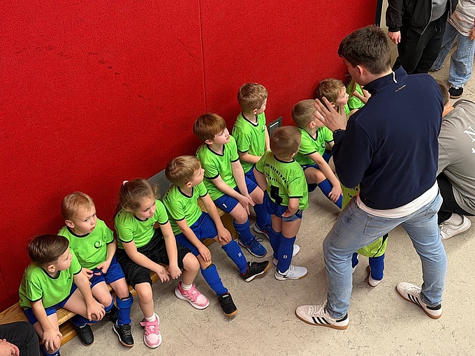 Die Mannschaft sitzt in Trikots auf einer Bank und bespricht mit dem Trainer die Taktik.