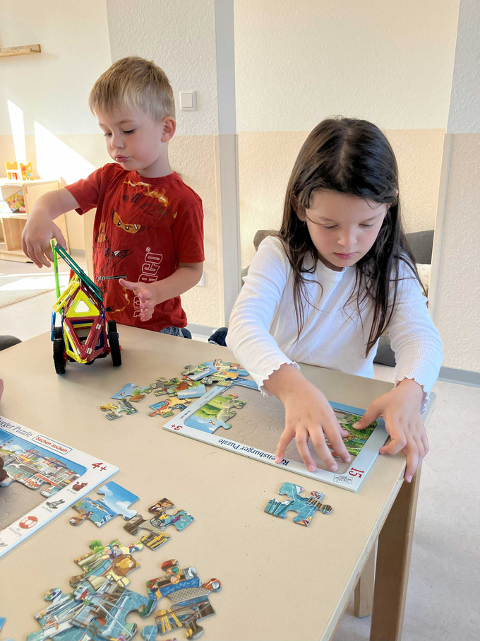 Ein Kind puzzelt, ein anderes spielt mit Magnetbausteinen.