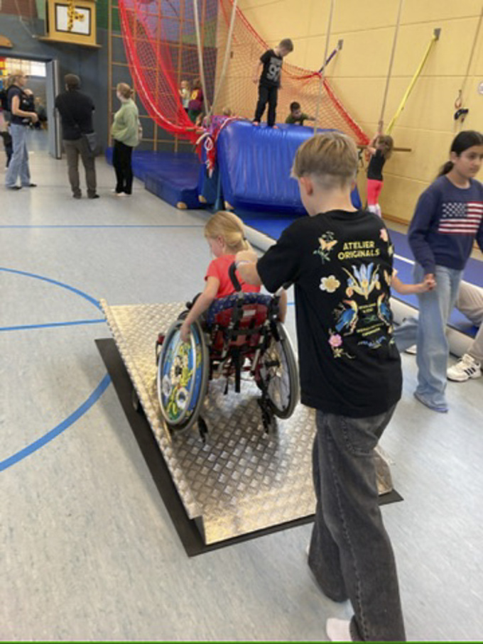 Ein Schüler schiebt ein Kind im Rollstuhl über eine Rampe.