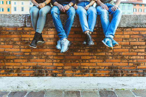 Junge Erwachsene sitzen auf einer Mauer, nur Füße und Beine sind zu sehen.