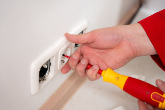 Eine Steckdose wird an die Wand geschraubt.