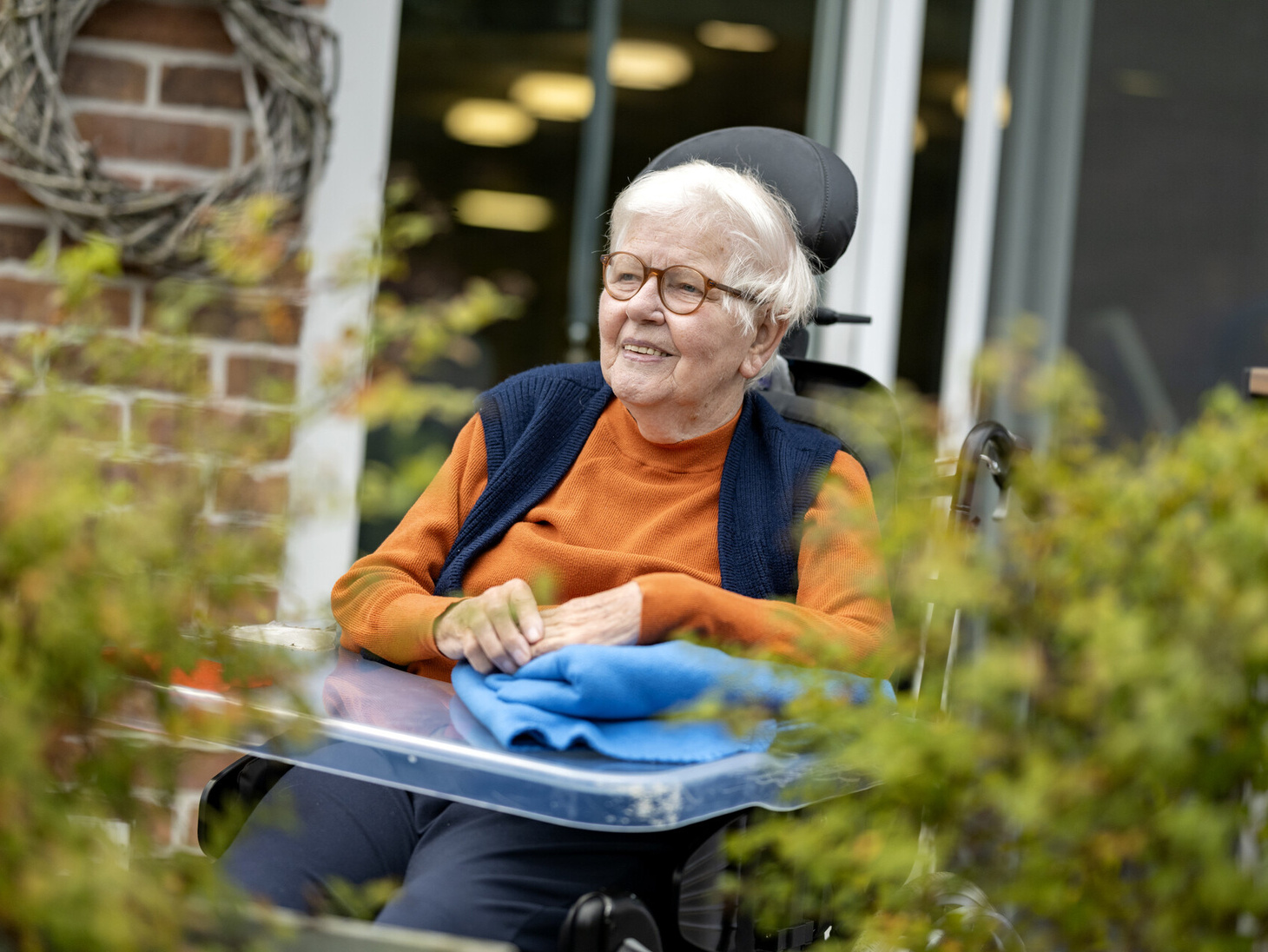 Eine ältere Person sitzt in einem elektrischen Rollstuhl auf einer Terasse.