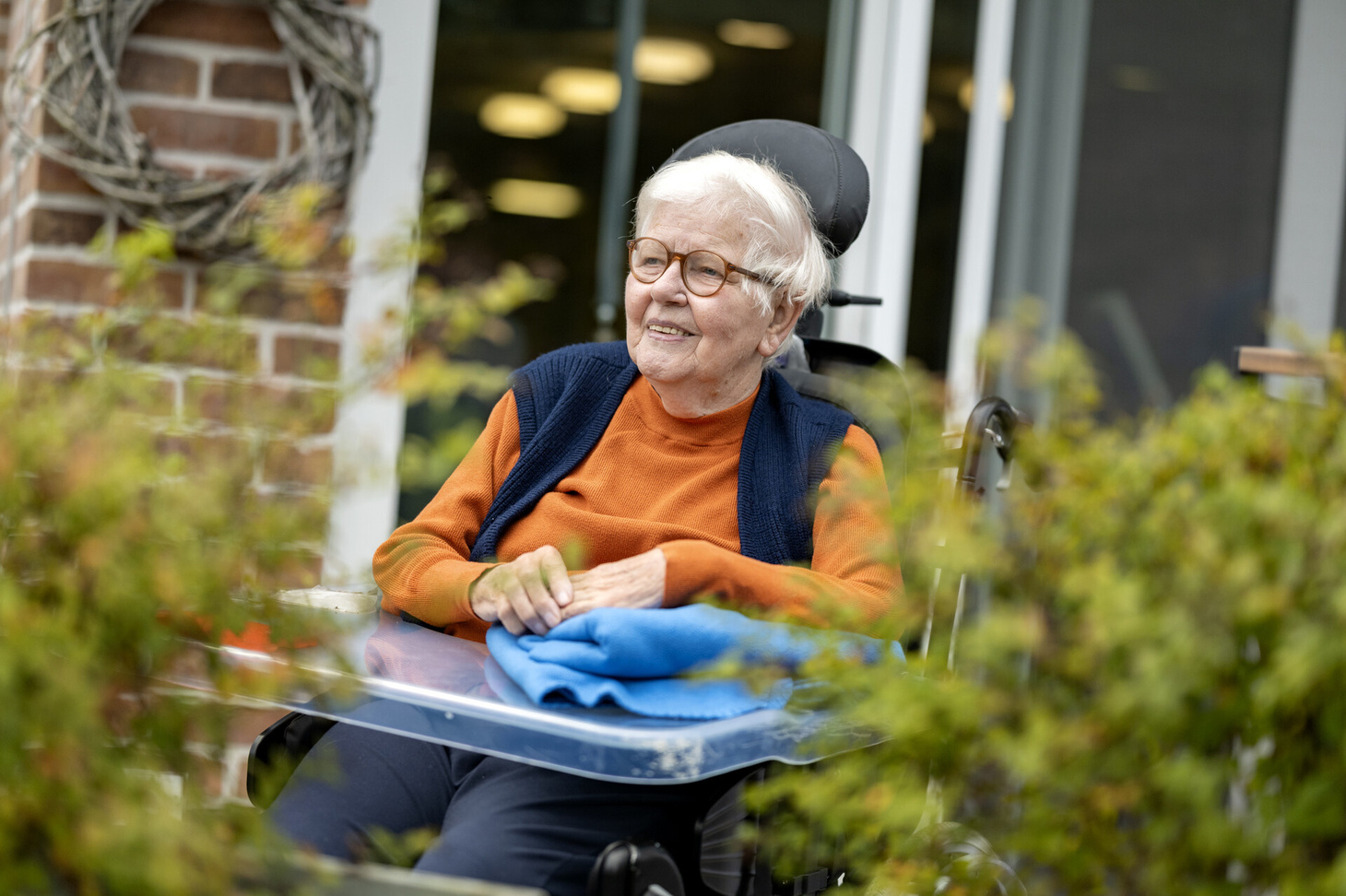 Eine ältere Person sitzt in einem elektrischen Rollstuhl auf einer Terasse.