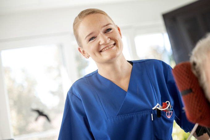 Mitarbeiterin in der Pflege schaut in die Kamera und lächelt