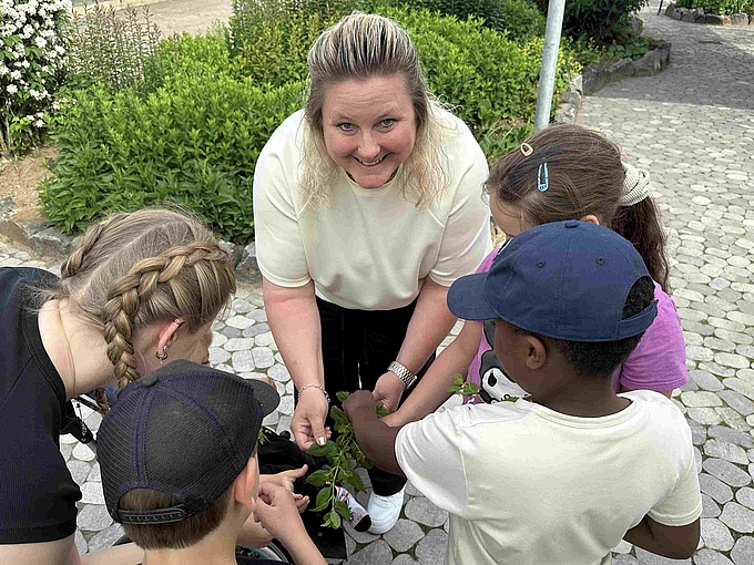 Zwei Erzieherinnen und mehrere Kinder riechen an Kräutern.