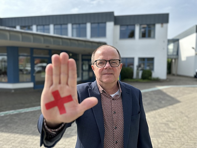 HpH-Geschäftsführer Guido Uhl zeigt ein rotes X, das Symbol der Kampagne "Nicht am Menschen sparen".