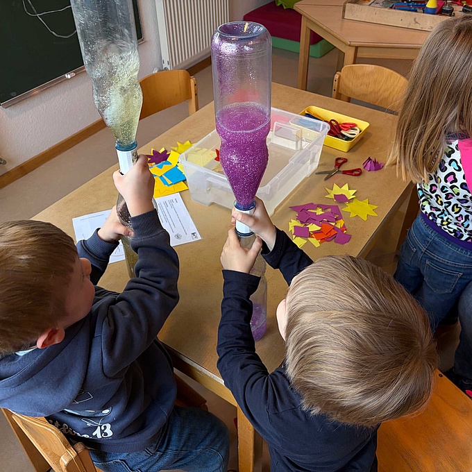 Zwei Kinder lassen in ihren Flaschen einen kleinen Strudel entstehen und beobachten, wie sich das Wasser wie ein Wirbel dreht.