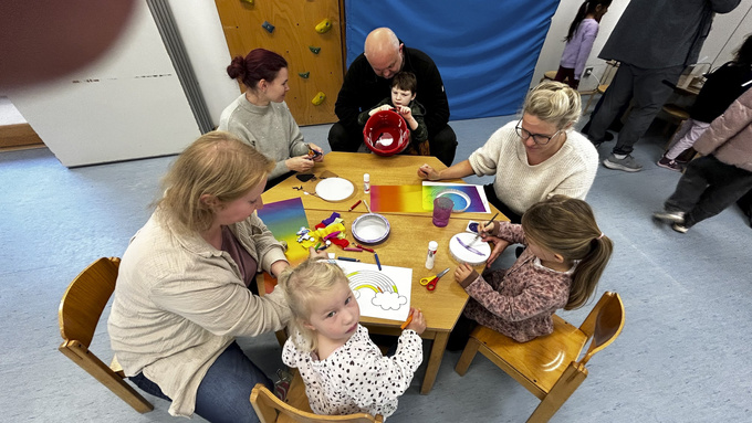 An einem Tisch sitzen mehrere Eltern und Kinder und basteln Laternen.