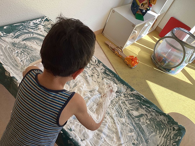 Ein Junge verteilt mit den Händen Rasierschaum auf einem Tisch.