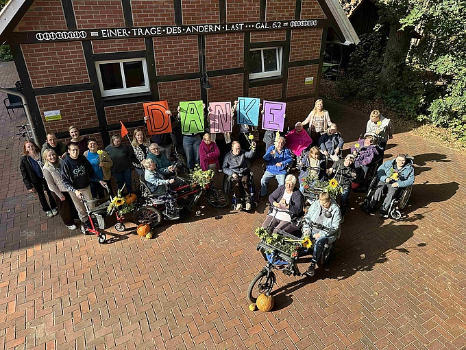 Die Bewohner von Haus Quadenort posieren mit dem neuen Fahrradanhänger und halten Blumen sowie Schilder mit der Aufschrift "Danke" in die Luft.