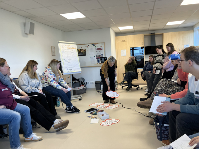 Eine Grupppe befindet sich in einem Raum und die Frau in der Mitte legt eine Moderationskarte auf den Boden.