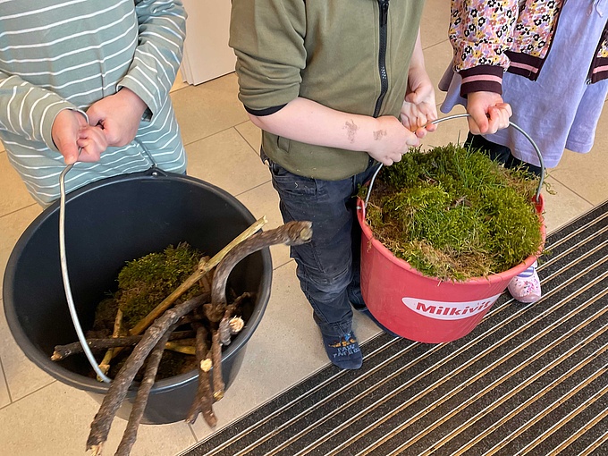 Zwei Kinder präsentieren das gesammelte Material für das Osternest: Äste und Moos.