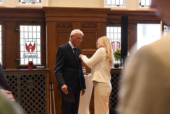 Anna Kebschull steckt Karl-Heinz Schnebel das Bundesverdienstkreuz ans Revers.