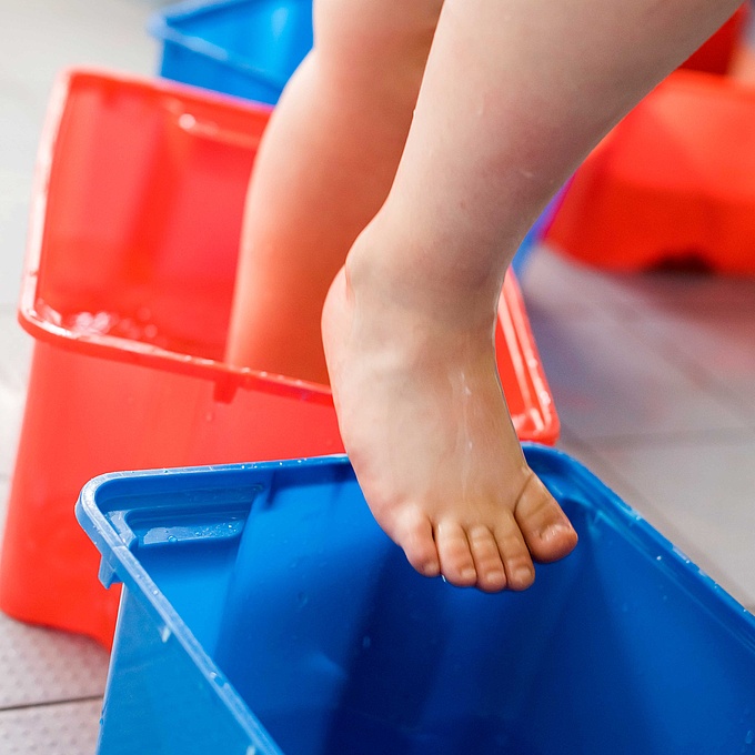 Ein Kind beim Wassertreten nach Kneipp: Das Kind geht mit den Füßen abwechselnd in Schüsseln mit kaltem und warmem Wasser.