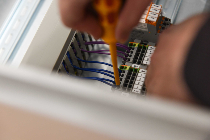 Herr Neufeld schraubt Kabel in einem Schaltkasten an.