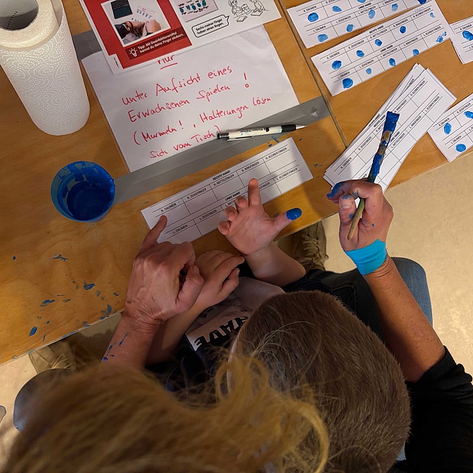 Ein Kind und eine Erzieherin machen einen Fingerabdruck.