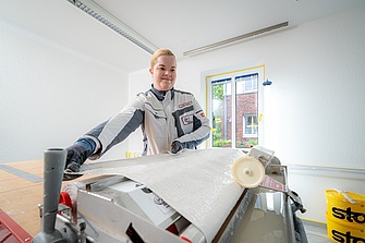 Malerin beim Tapezieren mit Tapeziermaschine
