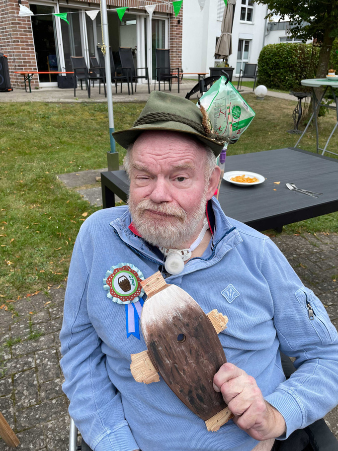 Der neue Schützenkönig, Bewohner Johannes Köhler, hält den Rumpf des Adlers in die Kamera. Auf dem Kopf trägt er einen Schützenhut. 