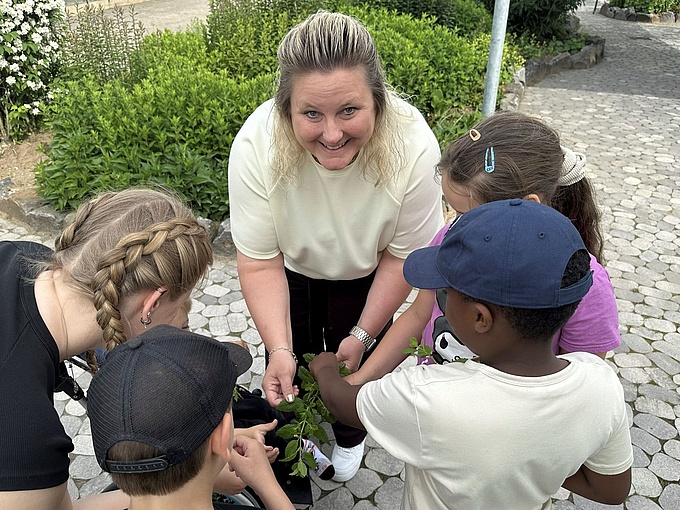 Zwei Erzieherinnen und mehrere Kinder bei der Kräuter-Ernte.