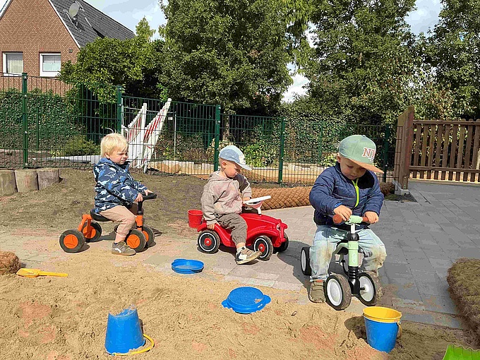 Mehrere Kinder spielen mit Baggern und anderen Geräten im Sandkasten.