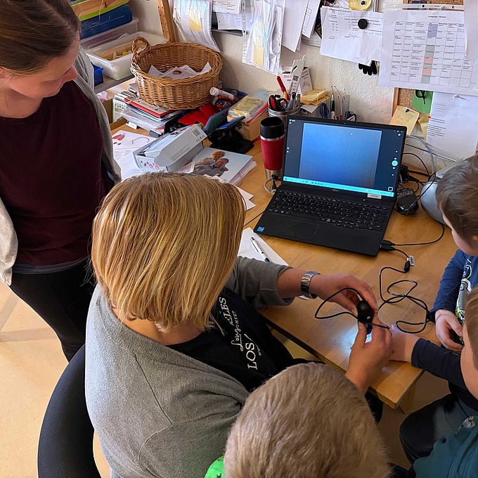 Erzieherinnen und Kinder untersuchen mit einer Digital-Mikroskop-Kamera die Hand eines Kindes.und weitere Körperteile intensiv betrachtet.